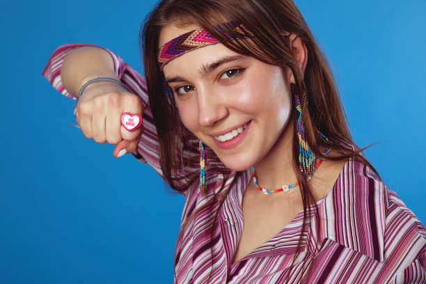 可爱的年轻嬉皮女孩在粉红色衬衫显示心形戒指，孤立在蓝色背景图片下载