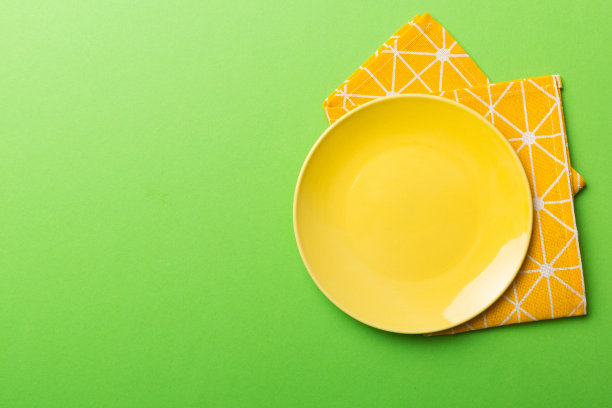 在彩色背景上的俯视图空圆形黄色盘子在桌布上的食物。空盘子放在餐巾上，为你的设计留出空间图片下载