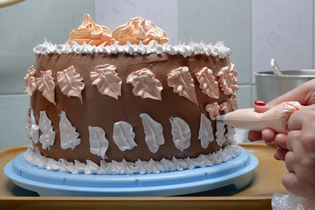 在家庭厨房里，一位女糕点师手里拿着一个糕点袋，在蛋糕上挤奶油。专业厨师在面包店厨房工作。烹饪，烘焙和烹饪概念食品，家庭烹饪图片下载