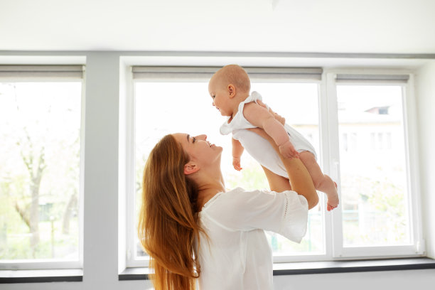 快乐开朗的年轻妈妈把一个可爱的婴儿抛向空中，玩耍，用爱和关怀拥抱婴儿图片下载