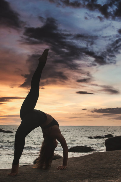 年轻女子在热带海岸线上做瑜伽姿势劈叉或麻绳，以保持健康的生活方式图片下载