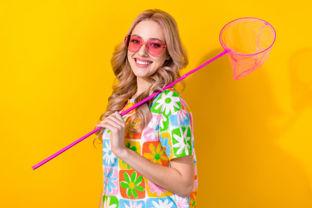 照片的漂亮少女可爱的女孩穿着彩色t恤，太阳镜蝴蝶网在肩上孤立的黄色背景图片下载