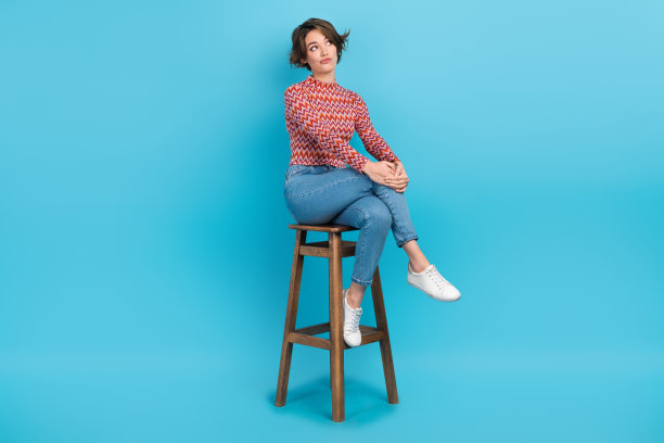 深思熟虑的可疑女士的全身照片，穿着粉红色的衬衫，坐在酒吧椅子上，看着空旷的空间孤立的蓝色背景图片下载