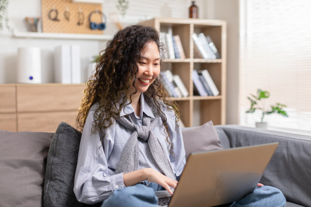 美丽的亚洲年轻女子穿着休闲，坐在沙发上，使用电脑笔记本电脑，娱乐社交媒体，放松，微笑和大笑。从事在线销售营销的自由职业女性。在家网上购物图片下载