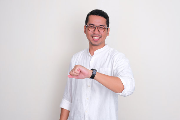 成年亚洲男子笑着开心，同时展示他的手臂手表图片下载