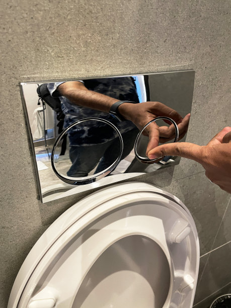 豪华酒店浴室的特写图片，棕色的石头瓷砖墙壁，墙上安装了闪亮的镀铬双冲水板，白色的陶瓷马桶盖，无法识别的人按按钮冲厕所图片下载