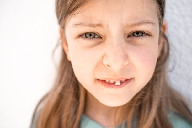 迷人的微笑小女孩孩子张开嘴，摇摇晃晃地松掉第一颗乳牙。学龄前儿童的牙齿在变。健康的口腔卫生。失去了牙齿。牙医治疗图片下载