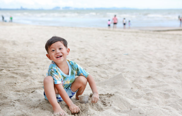 微笑的亚洲小男孩在沙滩上挖沙子玩得很开心。图片下载