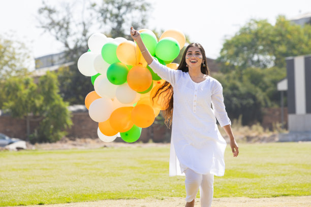 美丽快乐的年轻印度妇女穿着传统的白色连衣裙，在公园里拿着三色气球跑步，庆祝独立日或共和国日的概念。图片下载