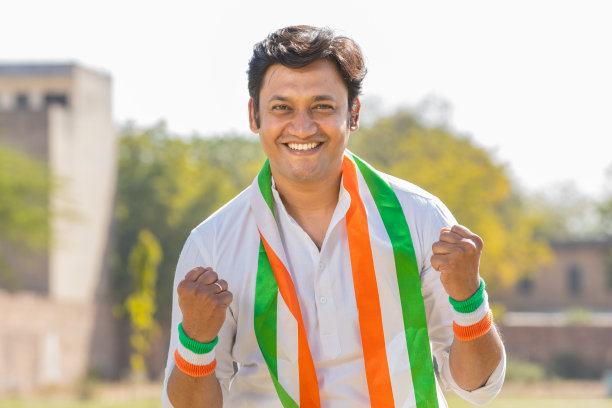 一个穿着传统的白色kurta和三色duppata站在公园里的快乐英俊的年轻人的肖像。球迷为印度队庆祝独立日或共和国日欢呼。图片下载