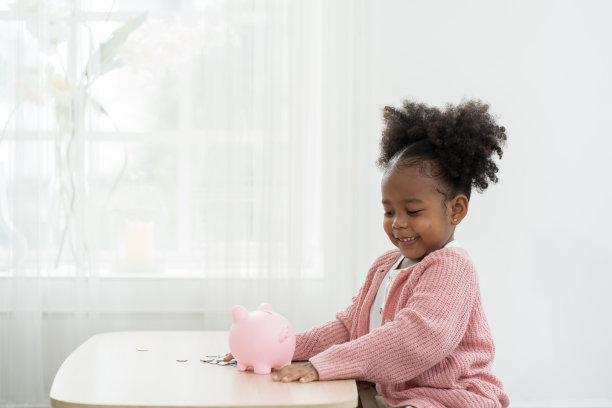 储蓄和银行理财的概念。小女孩往储蓄罐里存钱。非洲裔美国小女孩把一枚硬币放进存钱罐里。儿童投资未来概念图片下载