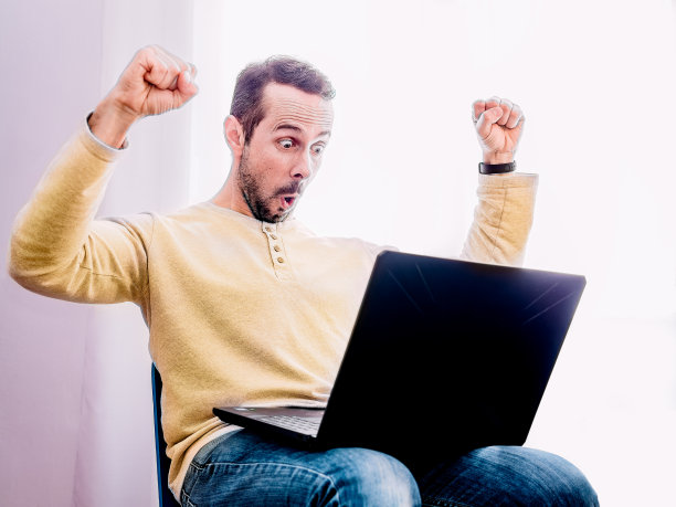 快乐兴奋的人拿着笔记本电脑，举起手臂庆祝成功或成就。图片下载