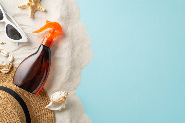 保护你的皮肤免受紫外线的伤害。头顶拍摄的防晒油喷雾瓶没有标签，周围是眼镜，帽子，贝壳手镯，海星在柔和的蓝色和沙质背景，文字或广告的空间图片下载
