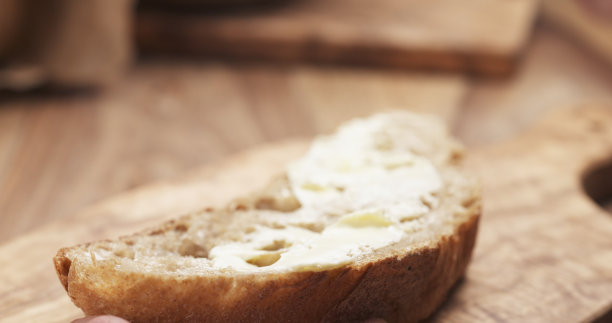 少女用手将黄油涂在一片质朴的面包上图片下载