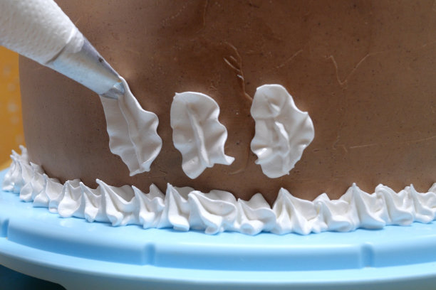 在家庭厨房里，一位女糕点师手里拿着一个糕点袋，在蛋糕上挤奶油。专业厨师在面包店厨房工作。烹饪，烘焙和烹饪概念食品，家庭烹饪图片下载