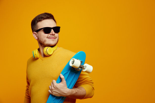 酷酷的家伙穿着黄色的套头衫，戴着墨镜，拿着长板，看着空旷的空间图片下载