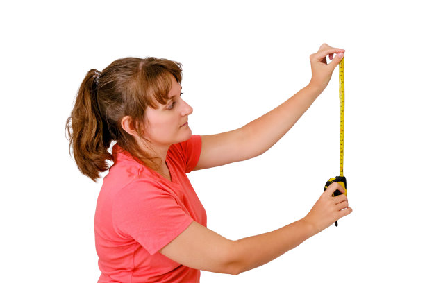 一个年轻的女人在白色的背景上测量房子里的墙。新公寓装修时的测量。图片下载