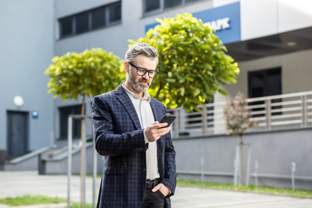 思考严肃、专注的成熟商人在手机上使用应用程序，高级老板拿着智能手机在城里闲逛，阅读新闻，上网浏览网页图片下载