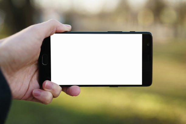 男子手持智能手机与白色屏幕户外与春天模糊的背景图片下载