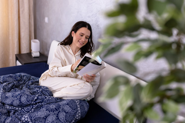 一位年轻女子正在一张舒适的现代床上看书。图片下载