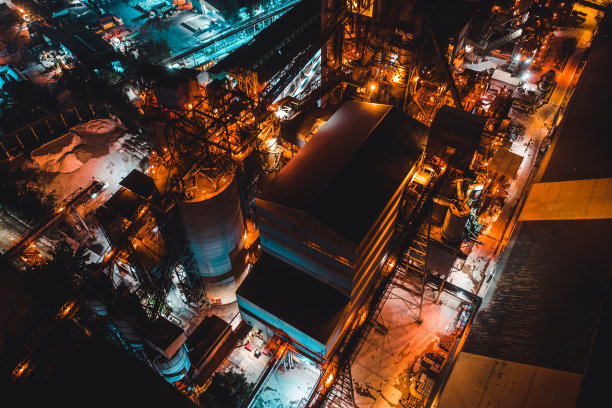 一座水泥厂的建筑在夜晚，一盏灯的灯光照亮了一座工厂。工业设施图片下载