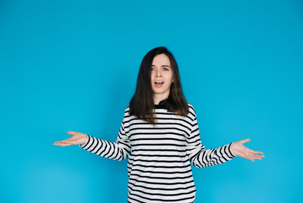 迷人的肖像惊讶的女人在条纹套头衫-惊讶和惊讶的女性模型与手臂延伸-孤立的蓝色背景-完美的表达震惊，惊喜和情感图片下载