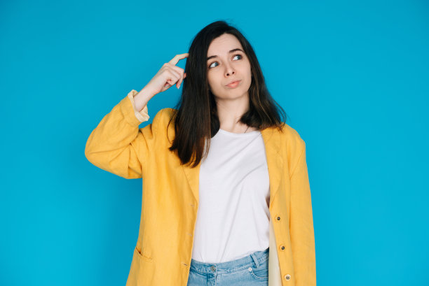 聪明的女商人摆出一副若有所思的姿势——撅着嘴挠着头的职业女性。一个聪明和有思想的商业女士的概念形象。非常适合做广告。蓝色背景图片下载