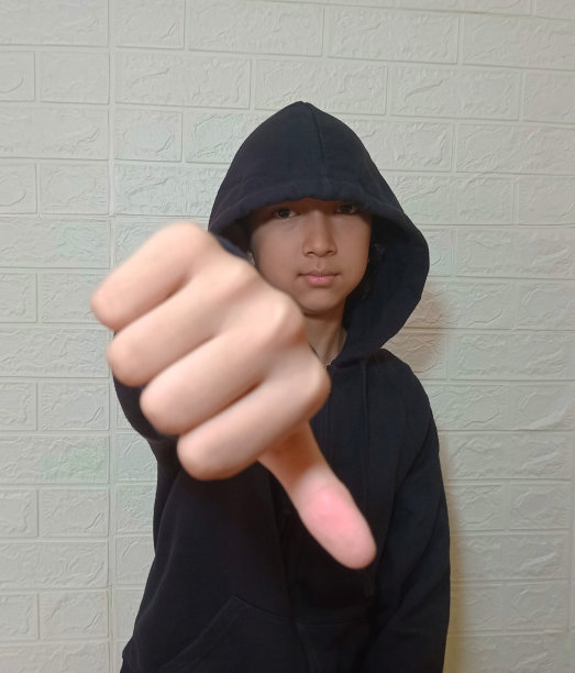 一个十几岁的女孩穿着连帽衫，在摄影棚里对着镜头摆姿势。
那个人看着相机，拇指朝下。图片下载