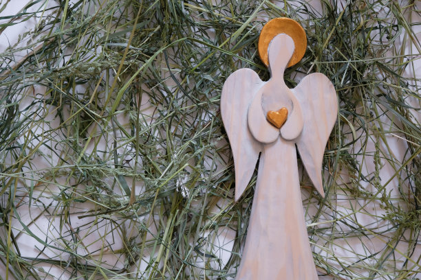 手执心脏，头戴金色光环的木制天使。绿色的干草。图片下载