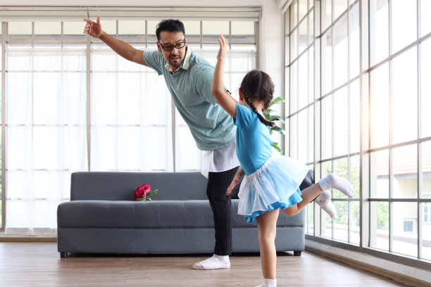 可爱的小女孩和年轻开朗帅气的爸爸穿着漂亮的裙子一起跳舞，爸爸努力训练女儿跳芭蕾，一家人欢天喜地地在一起度过时光。祝您父亲节快乐。图片下载