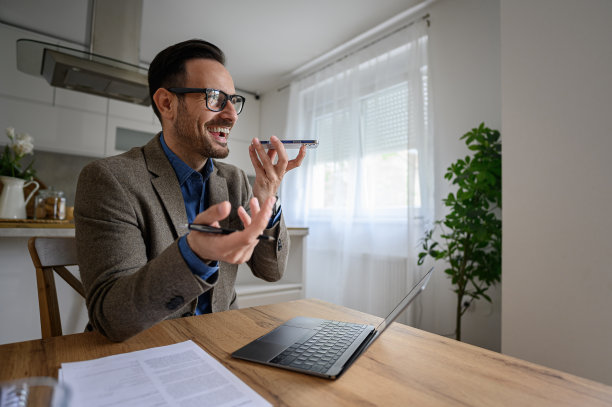 快乐的男性专业人士在家庭办公室用智能手机扬声器和笔记本电脑说话图片下载