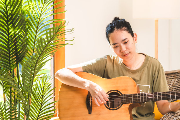 年轻的亚洲女性在家里学习吉他，舒适的家庭室内有阳光放松家庭生活方式，吉他手享受在客厅弹吉他图片下载