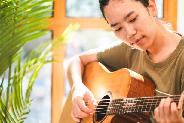 年轻的亚洲女性在家里学习吉他，舒适的家庭室内有阳光放松家庭生活方式，吉他手享受在客厅弹吉他图片下载