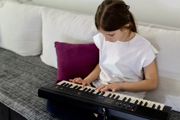 可爱的小女孩坐在家里的沙发上弹电子琴。图片下载