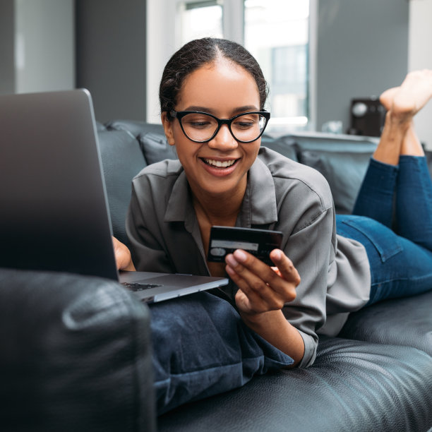 一个快乐的年轻女性拿着信用卡躺在客厅的沙发上的特写图片下载