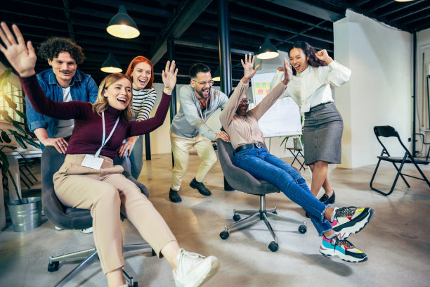 年轻开朗的商人们穿着漂亮的休闲装，在办公室椅子上赛跑，笑得很开心图片下载