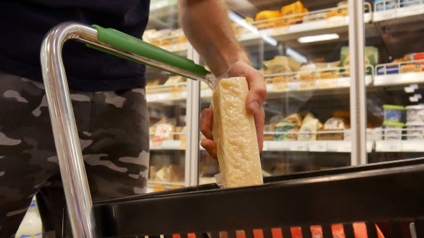 奶制品部购物车的特写镜头，一位男顾客正用手把一包奶酪放进购物车图片下载