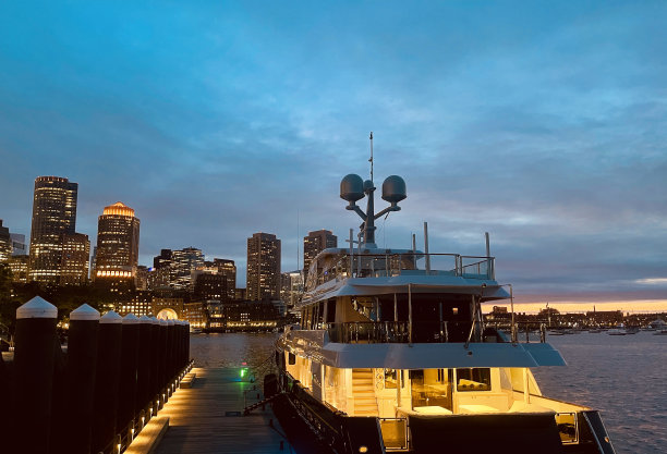 2023年6月，一艘豪华船在前面和马萨诸塞州波士顿市中心的日落傍晚照片，有高层建筑和水中的倒影图片下载