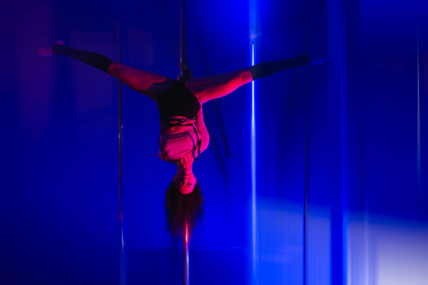体操女舞者在蓝色背景上倒立在杆子上劈叉。图片下载