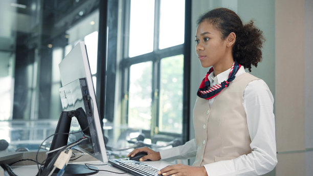 年轻的美籍非裔航空公司地勤人员，身着制服，在机场检票柜台操作电脑。航空公司值机柜台的地勤服务员图片下载