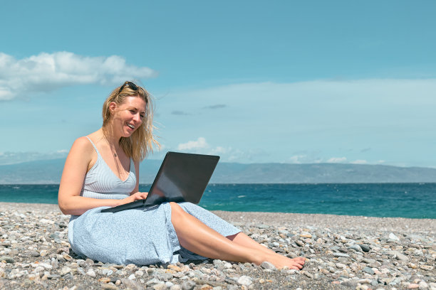金发美女在沙滩上用笔记本电脑。在户外工作的女商人。科技和旅游，自由职业者的概念。现代办公室。遥远的工作。图片下载