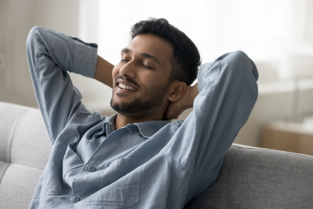 快乐放松英俊的印度人坐在舒适的沙发上图片下载