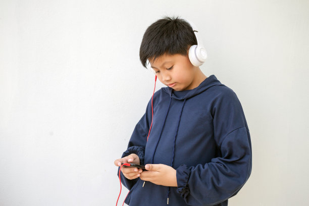 可爱的亚洲男孩穿着连帽衫摆姿势站着微笑，带着耳机听音乐。一个享受音乐的小男孩的情感画像图片下载