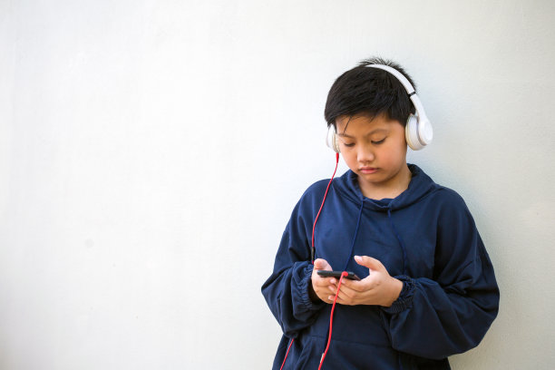 可爱的亚洲男孩，穿着连帽衫，皮肤白皙，在白色的背景下用手机和耳机听音乐。纵向和复制空间图片下载