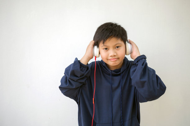可爱的亚洲男孩穿着连帽衫摆姿势站着微笑，带着耳机听音乐。一个享受音乐的小男孩的情感画像图片下载