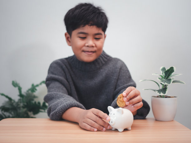 一个男孩把硬币放进扑满。学习财务责任和计划储蓄。储蓄的概念。投资的概念。图片下载