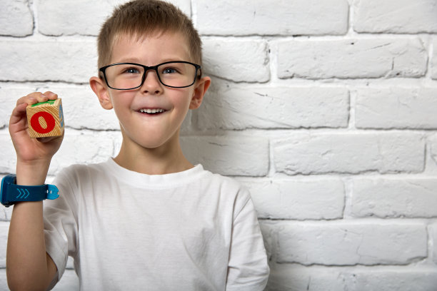 男孩站在白色的砖墙旁边，墙上有立方体，上面有彩色的字母和字母图片下载