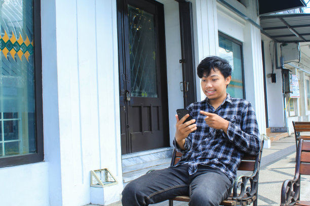 兴奋的年轻亚洲男子微笑着指着他的智能手机图片下载