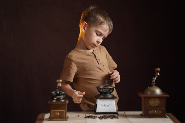 可爱的小男孩用复古咖啡研磨机研磨咖啡。图片下载