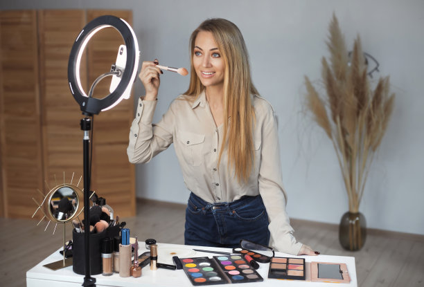 美丽的年轻金发美女博主用智能手机在线录制了一段视频，并提供了化妆教程。社交媒体和传播概念图片下载